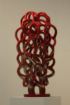 Sculpture décorative abstraite en nœuds de métal rouge sur socle blanc.