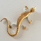 Sculpture de salamandre dorée sur fond clair, queue en boucle et détail des pattes