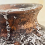 Gros plan sur le vase en terre cuite : surface brune patinée et zones blanchâtres.