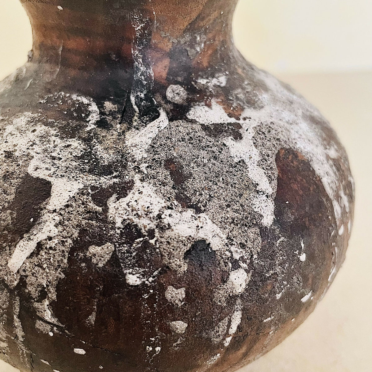 Gros plan sur le vase : matière brun foncé avec reliefs et éclats blanchâtres.