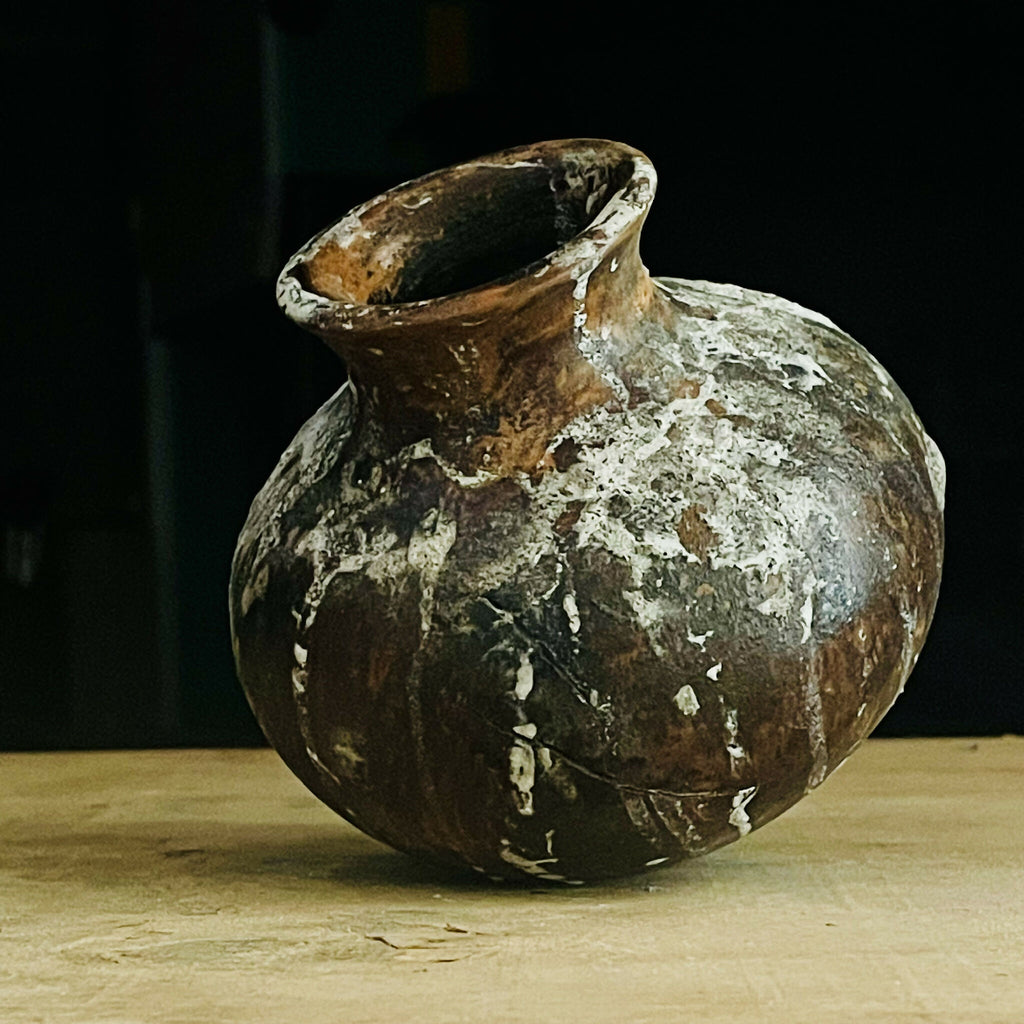 Vase en terre cuite brun, col évasé, aspect ancien avec dépôts blanchâtres.