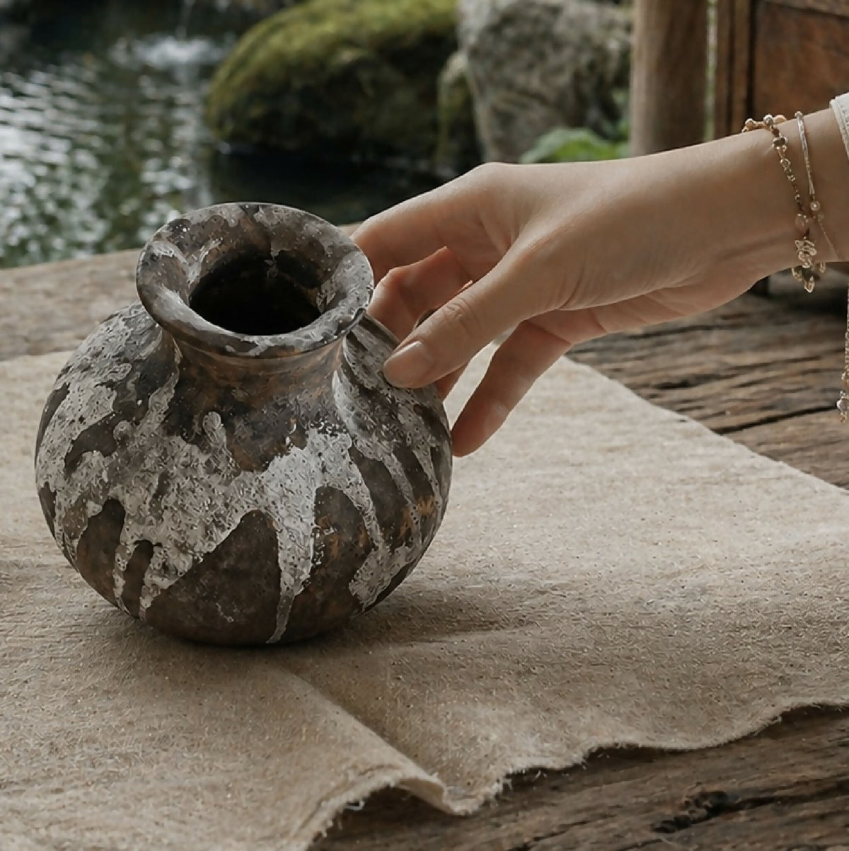 Petit vase en poterie brun gris, col court évasé, texture usée et éclats blanchâtres.