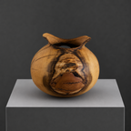 Vase en bois sculpté avec large ouverture sombre, nervures du bois et fentes.