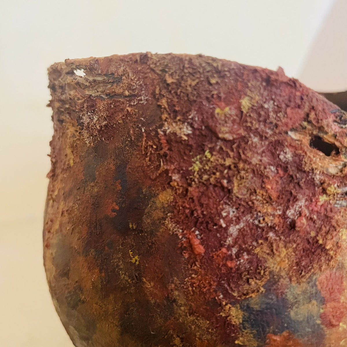 Vase en métal oxydé, gros plan sur la surface rugueuse avec zones claires et fissures.