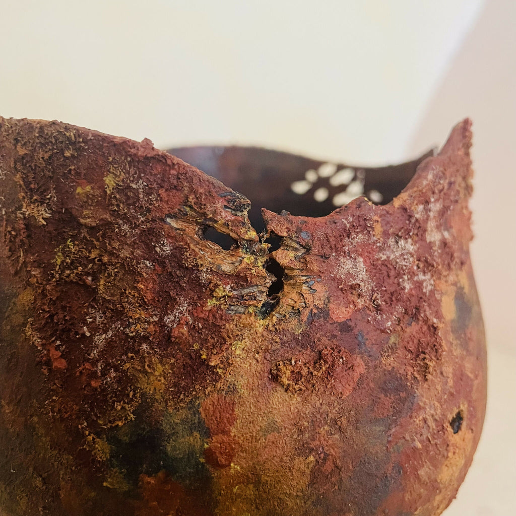 Vase en métal oxydé, gros plan du bord, paroi patinée avec trous et reliefs.