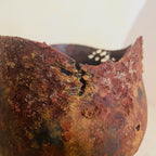 Vase en métal oxydé, gros plan du bord, paroi patinée avec trous et reliefs.