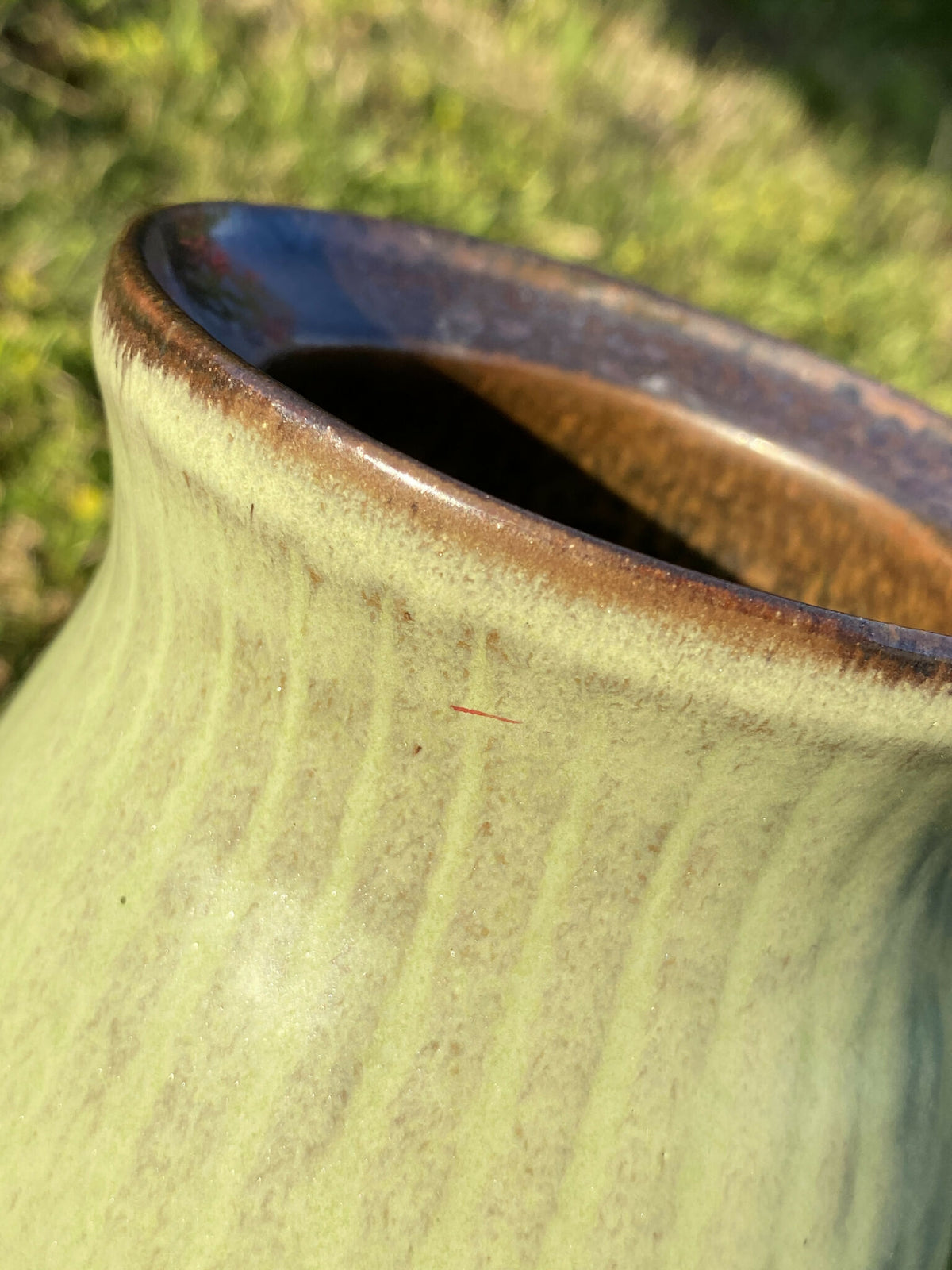 Vase en céramique vert clair, ouverture à bord bleu foncé, intérieur sombre.