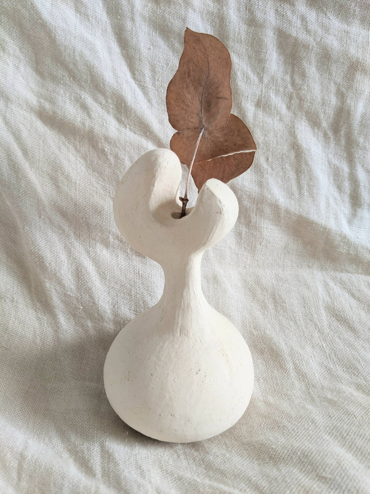 Vase en céramique blanche avec feuilles brunes séchées et tige centrale
