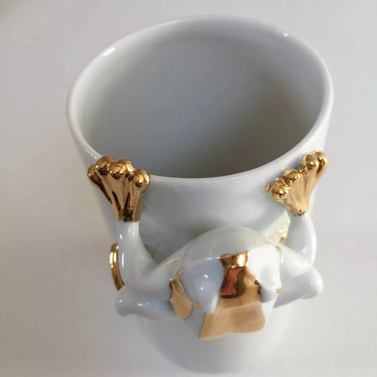 Vase en forme de grenouille blanc, vue intérieure avec pattes dorées.