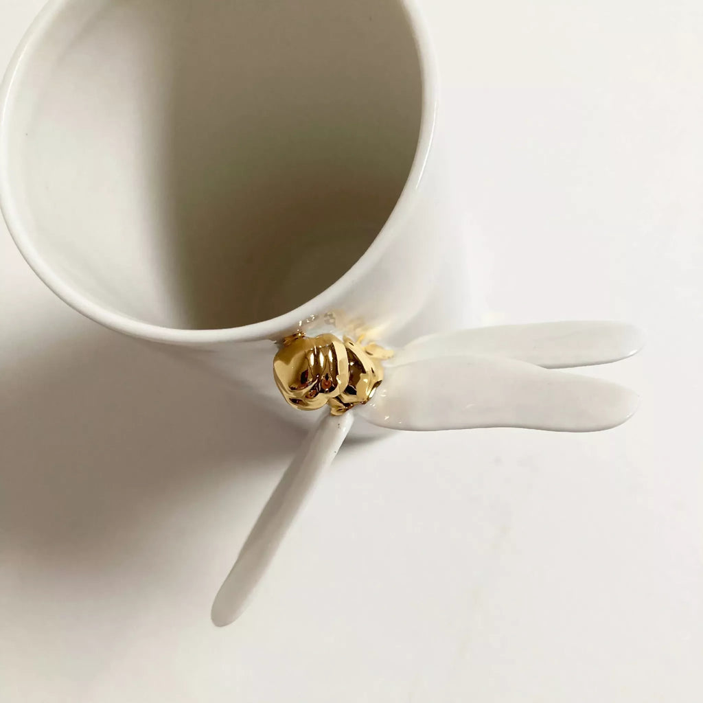 Vase blanc vu de côté, bouche ouverte, libellule blanche avec base dorée.
