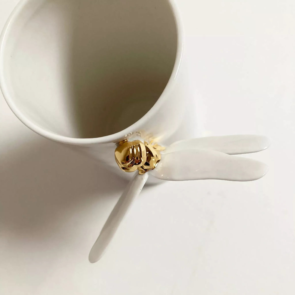 Vase blanc vu de côté, bouche ouverte, libellule blanche avec base dorée.