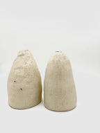 Deux vases coniques DUO beige, texture granuleuse et ouvertures noires en haut.
