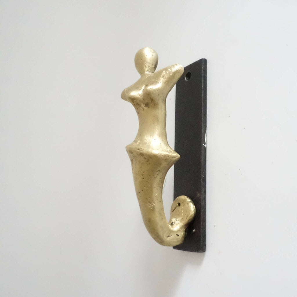 Porte-manteau mural avec patère en forme de figurine dorée sur plaque noire.