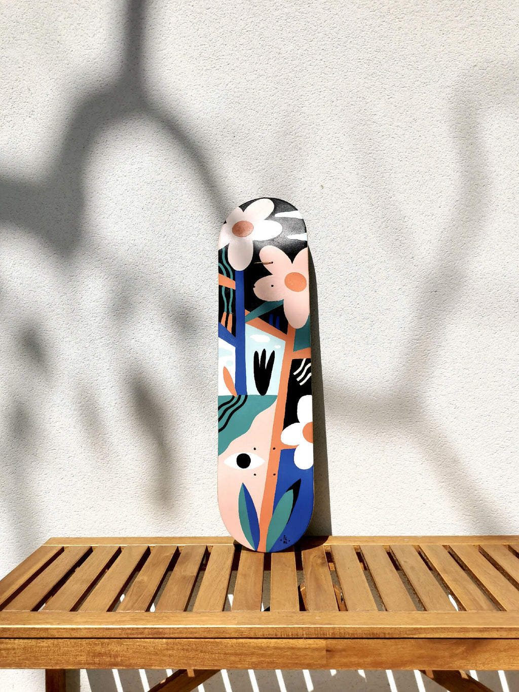 Skateboard vertical, illustré de visages stylisés et fleurs, motifs bleu, orange et noir.