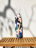 Skateboard vertical, illustré de visages stylisés et fleurs, motifs bleu, orange et noir.