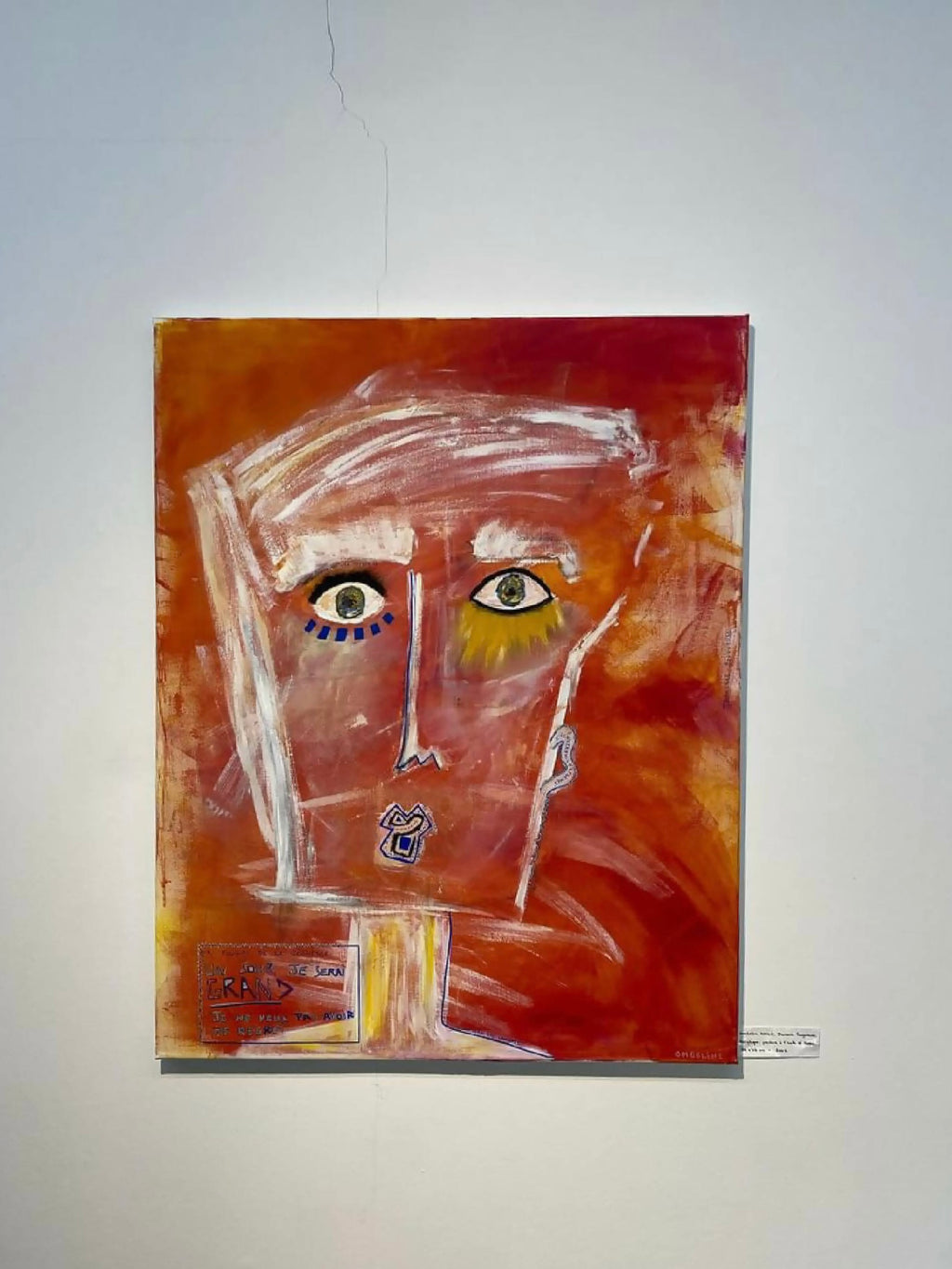 Peinture : visage abstrait sur fond rouge orangé, regard aux yeux bleus et jaunes.