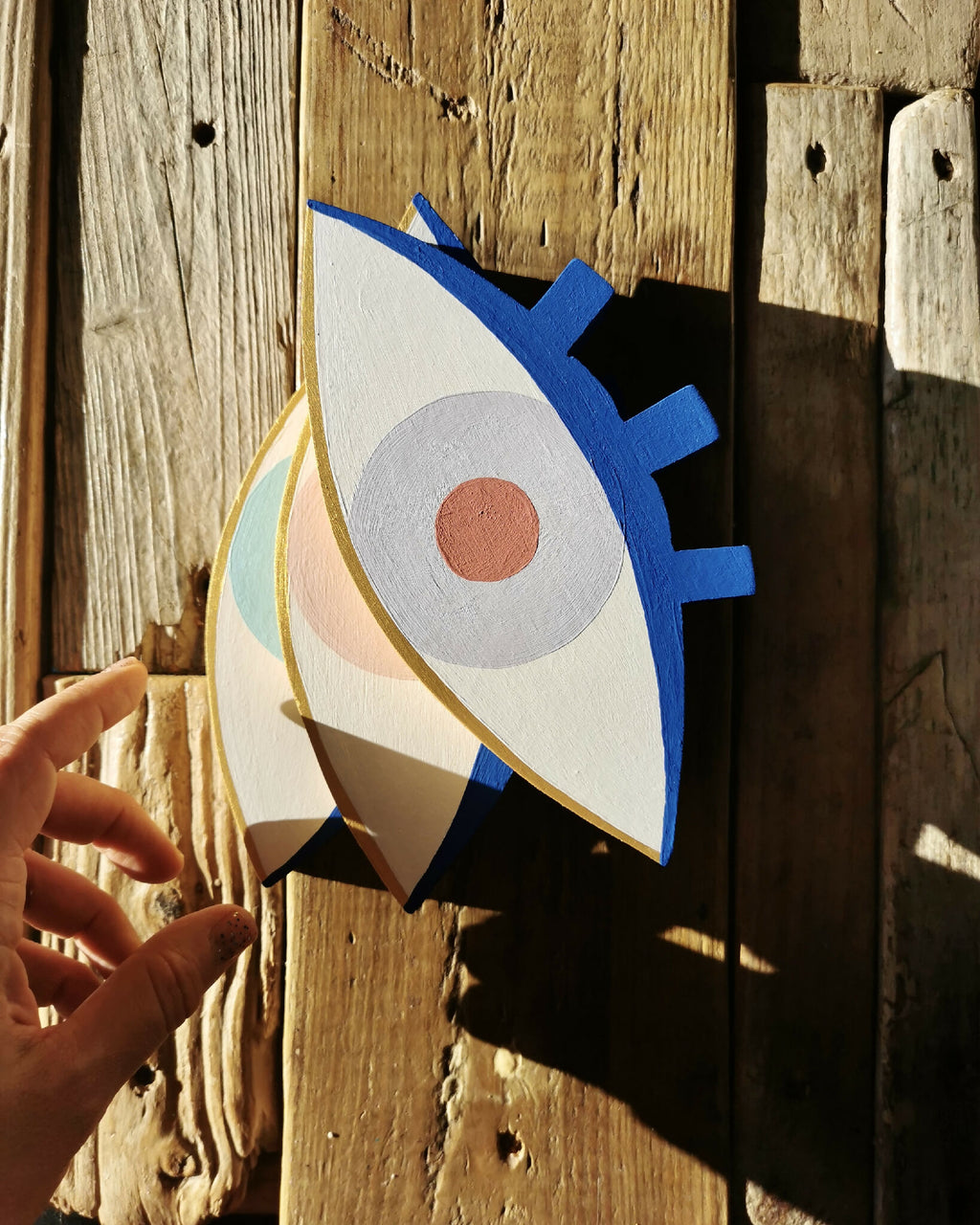 Œil en bois peint, contour bleu, iris bleu clair, pupille orange tenu à la main.