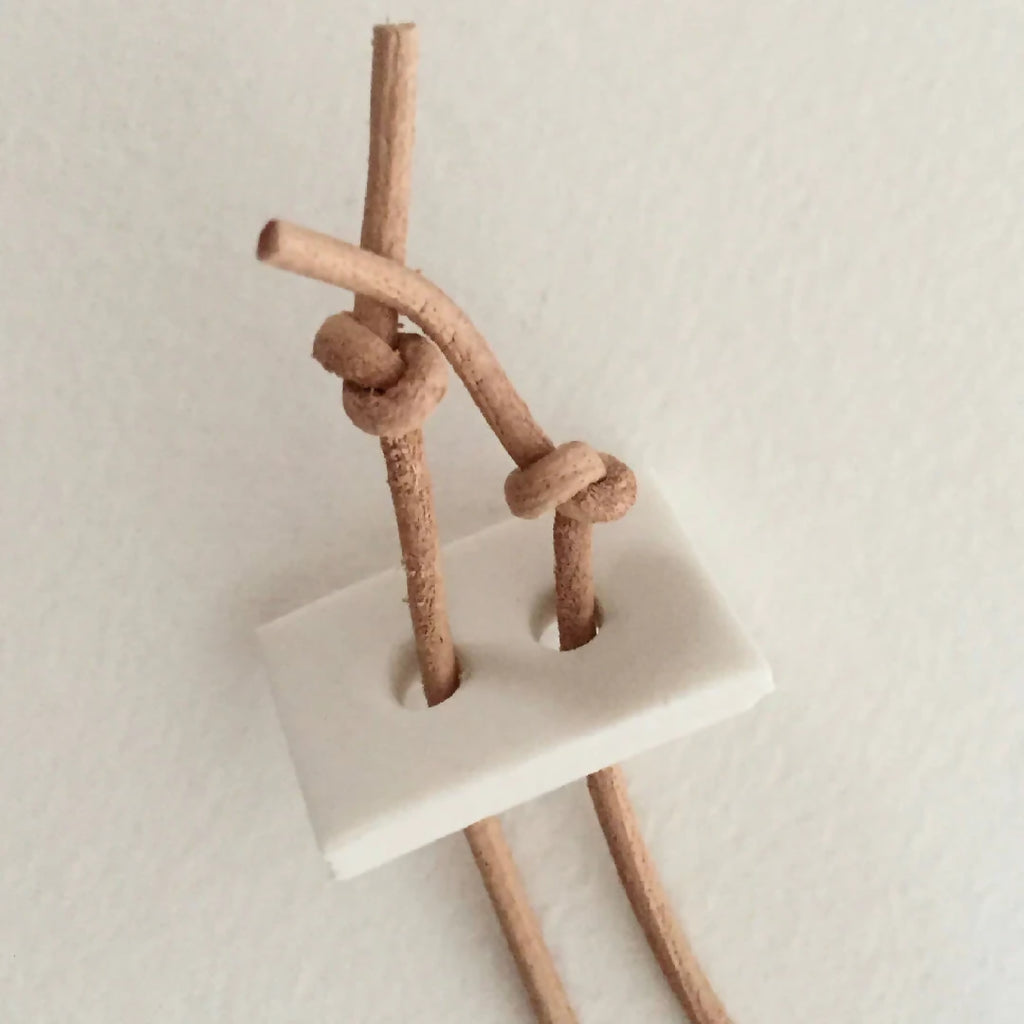 Pendentif en porcelaine blanche vu de côté, attache en cuir et cordon beige