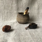 Petit pot en terre cuite gris foncé, forme arrondie évasée, surface texturée.