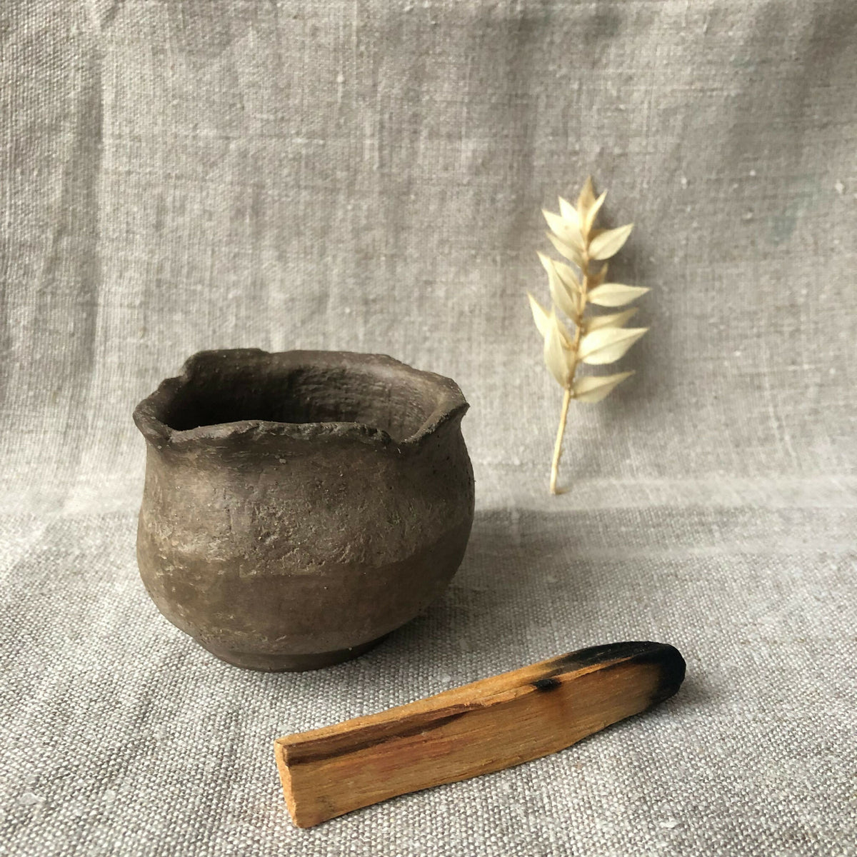 Petit pot en terre cuite gris, bord irrégulier, surface patinée, petite brindille.