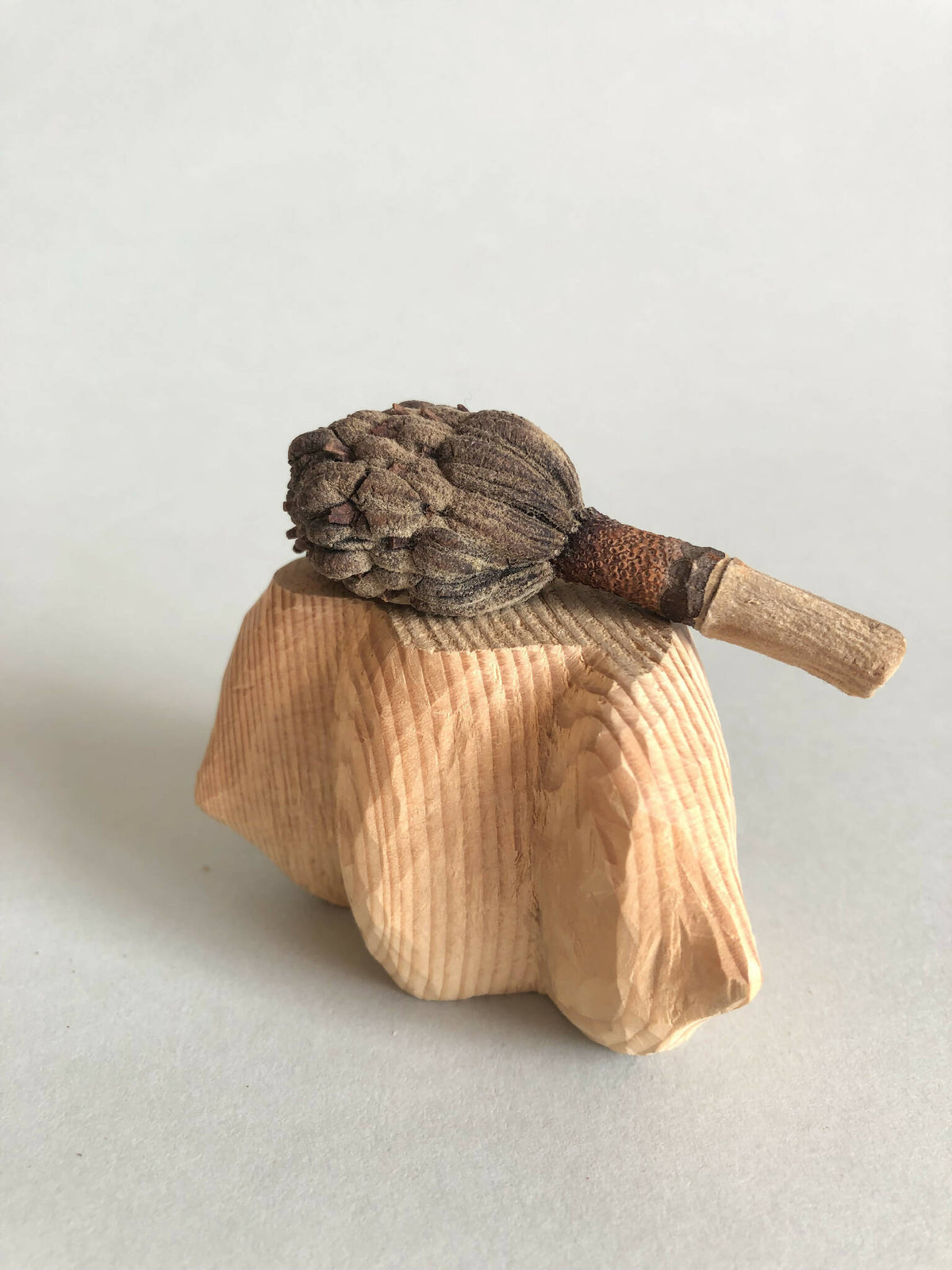 Petit socle sculpté beige avec figurine brune et petite tige, relief strié