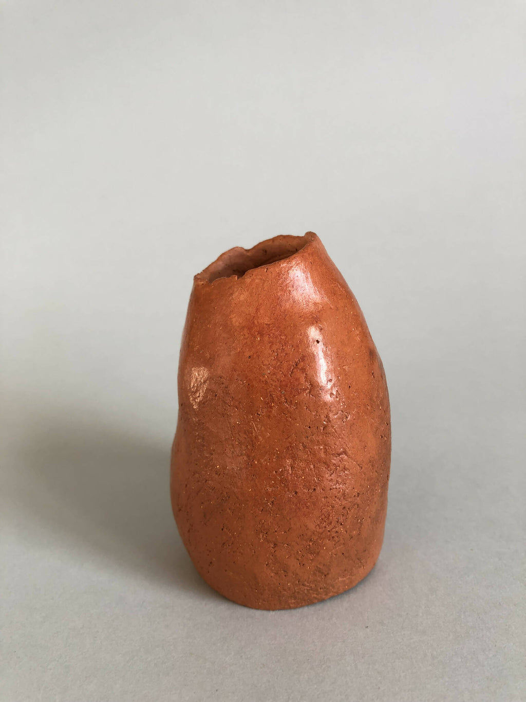 Petit vase en terre cuite orange, vue de côté, texture irrégulière.