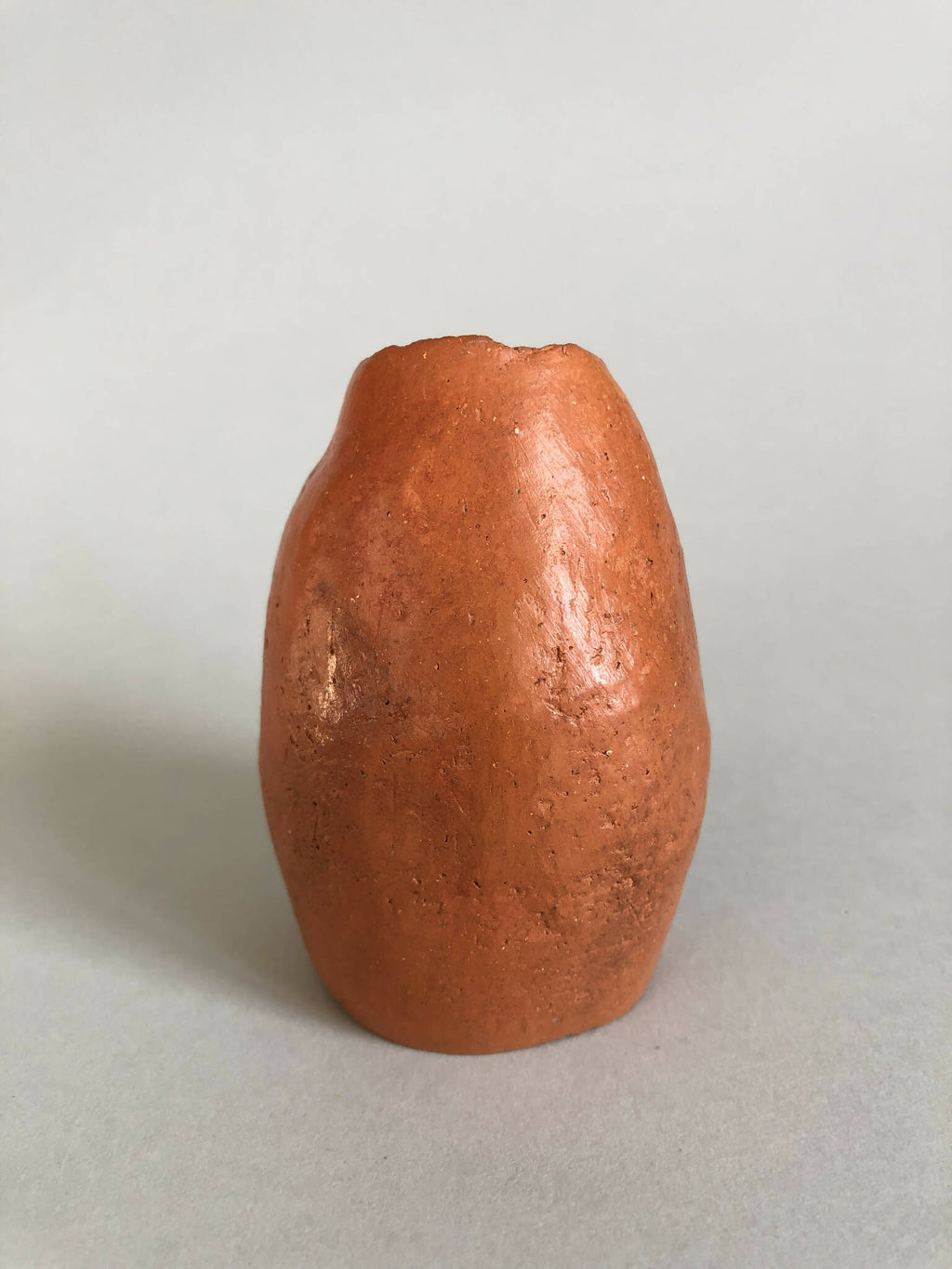 Petit vase en terre cuite orange, forme arrondie, surface granuleuse.