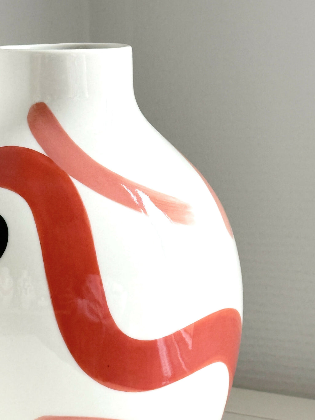 Petit vase buste blanc en vue rapprochée, motif rouge corail et trait rose.