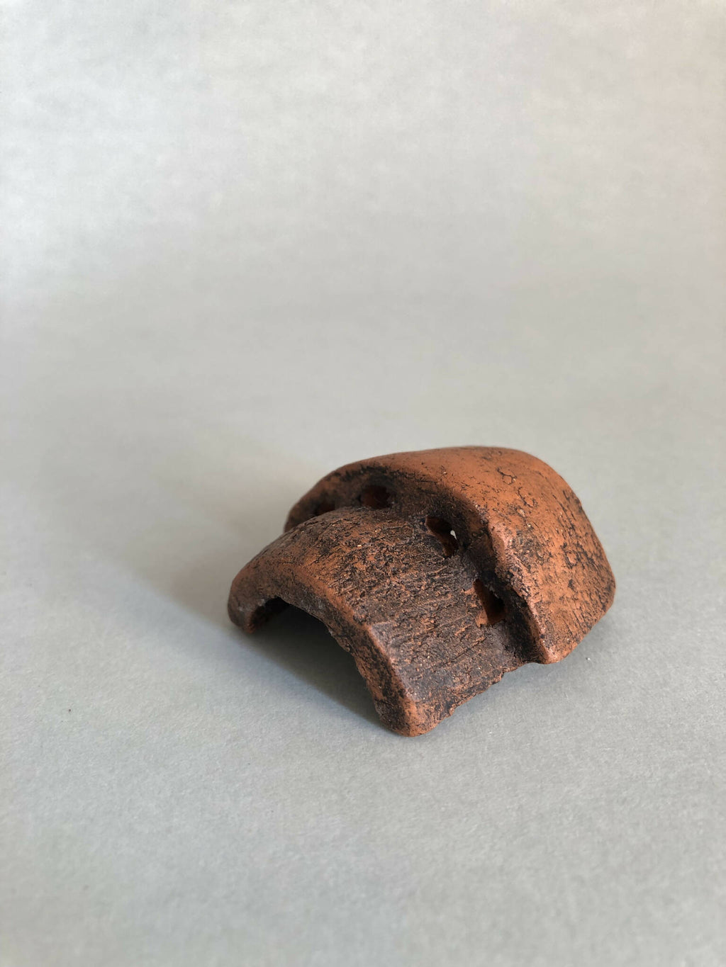 Petite pièce en cuivre rouillé ajourée, cavité concave, vue inclinée.