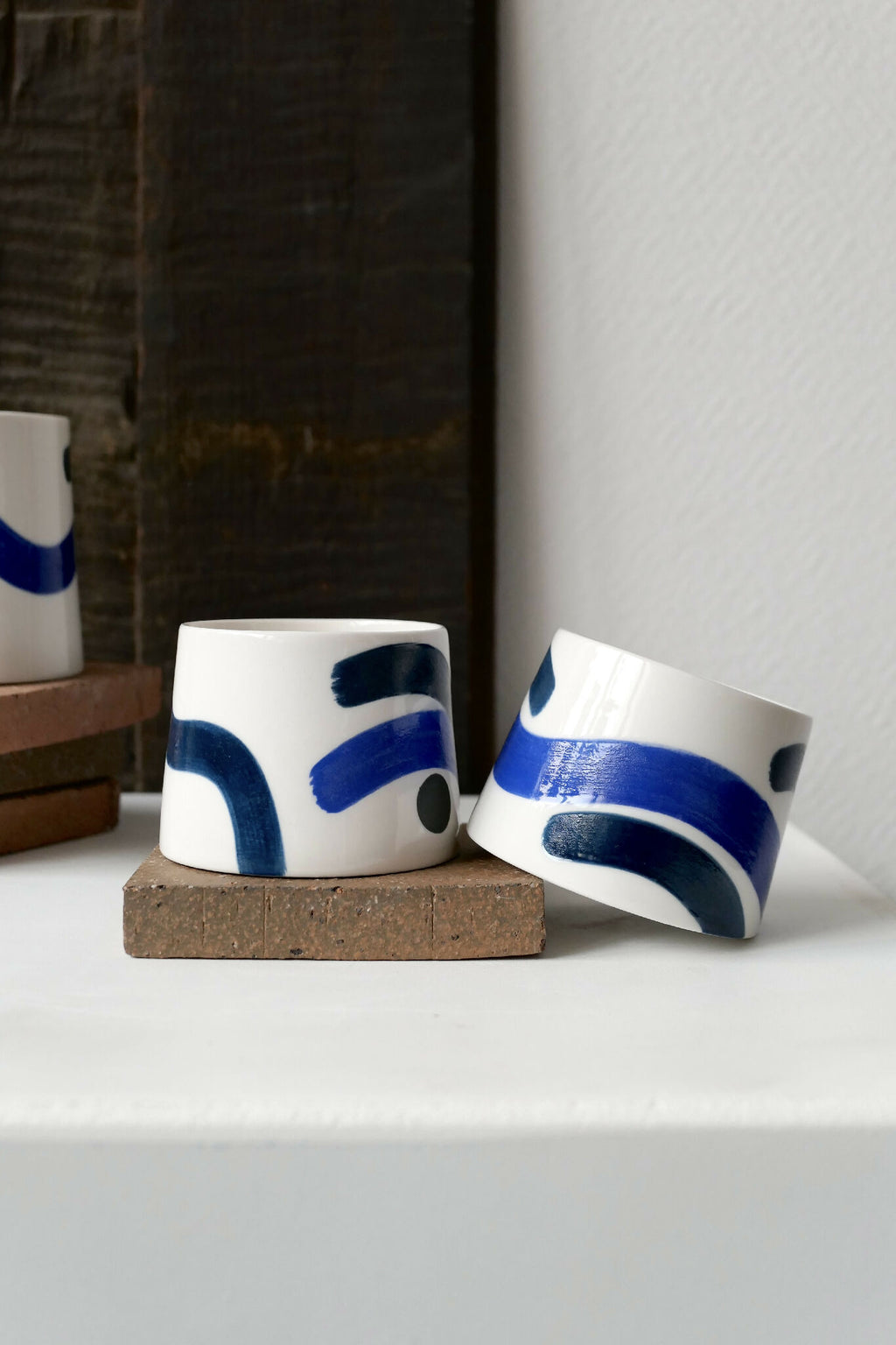 Petites tasses trapèzes blanches à motifs bleus, deux exemplaires sur socle.