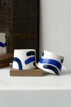 Petites tasses trapèzes blanches à motifs bleus, deux exemplaires sur socle.