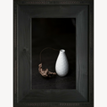 Cadre avec vase blanc texturé et branche de feuille morte séchée.