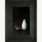 Cadre avec vase blanc texturé et branche de feuille morte séchée.