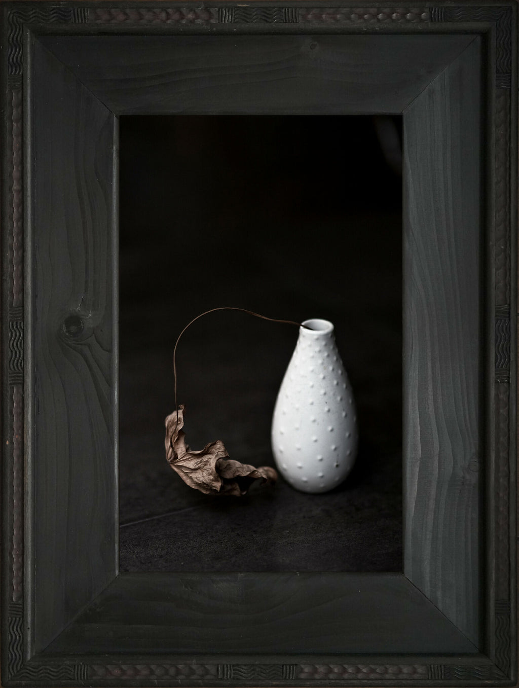 Cadre encadré avec vase blanc en céramique et branche de feuille morte séchée.