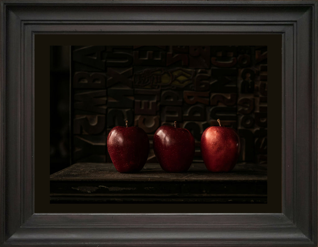 Nature morte encadrée : trois pommes rouges sur une table