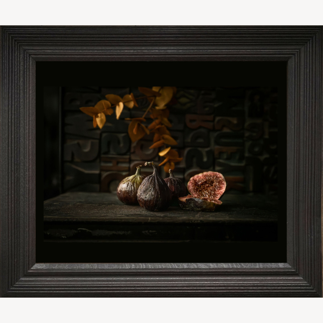 Tableau nature morte encadré montrant figues entières et figue tranchée sur socle sombre