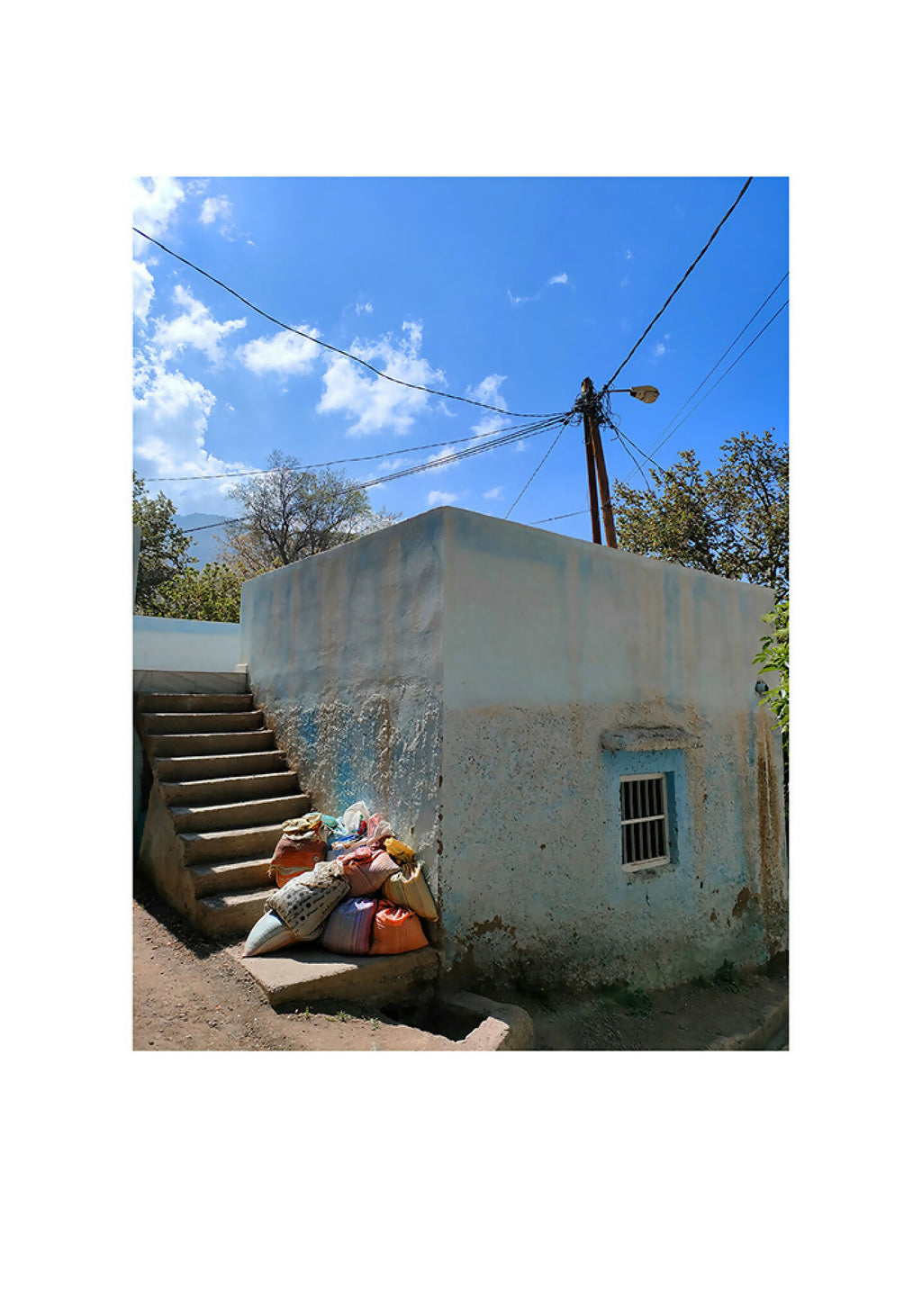 Photographie nature : ciel bleu, petite maison béton, fils électriques et deux personnes allongées