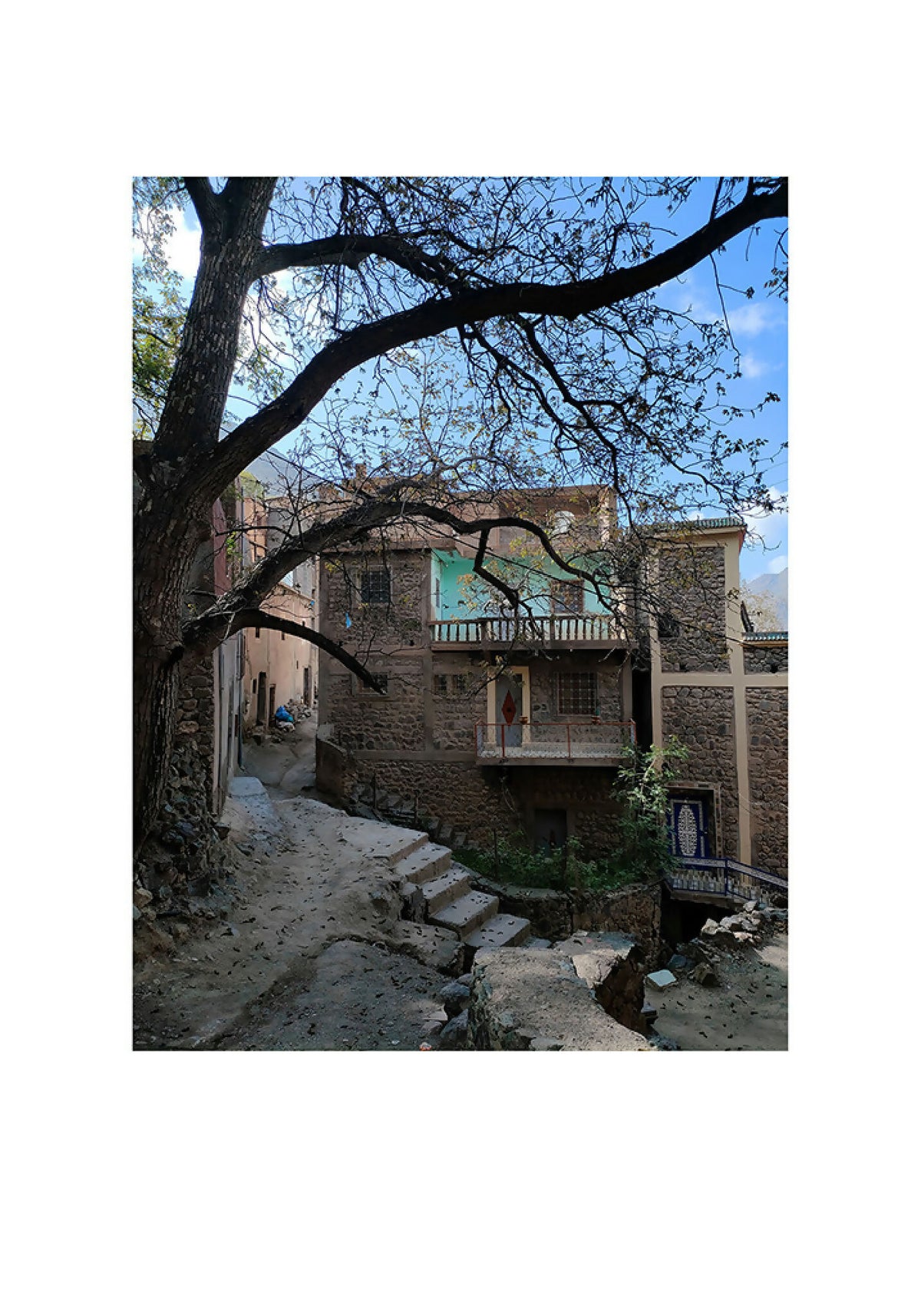 Tirage photo vertical : ruelle en pierre sous un ciel bleu, arbre aux branches.