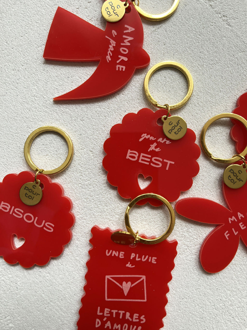 Ensemble de porte-clés rouges avec anneaux dorés, formes fleurs et carte, messages d’amour.