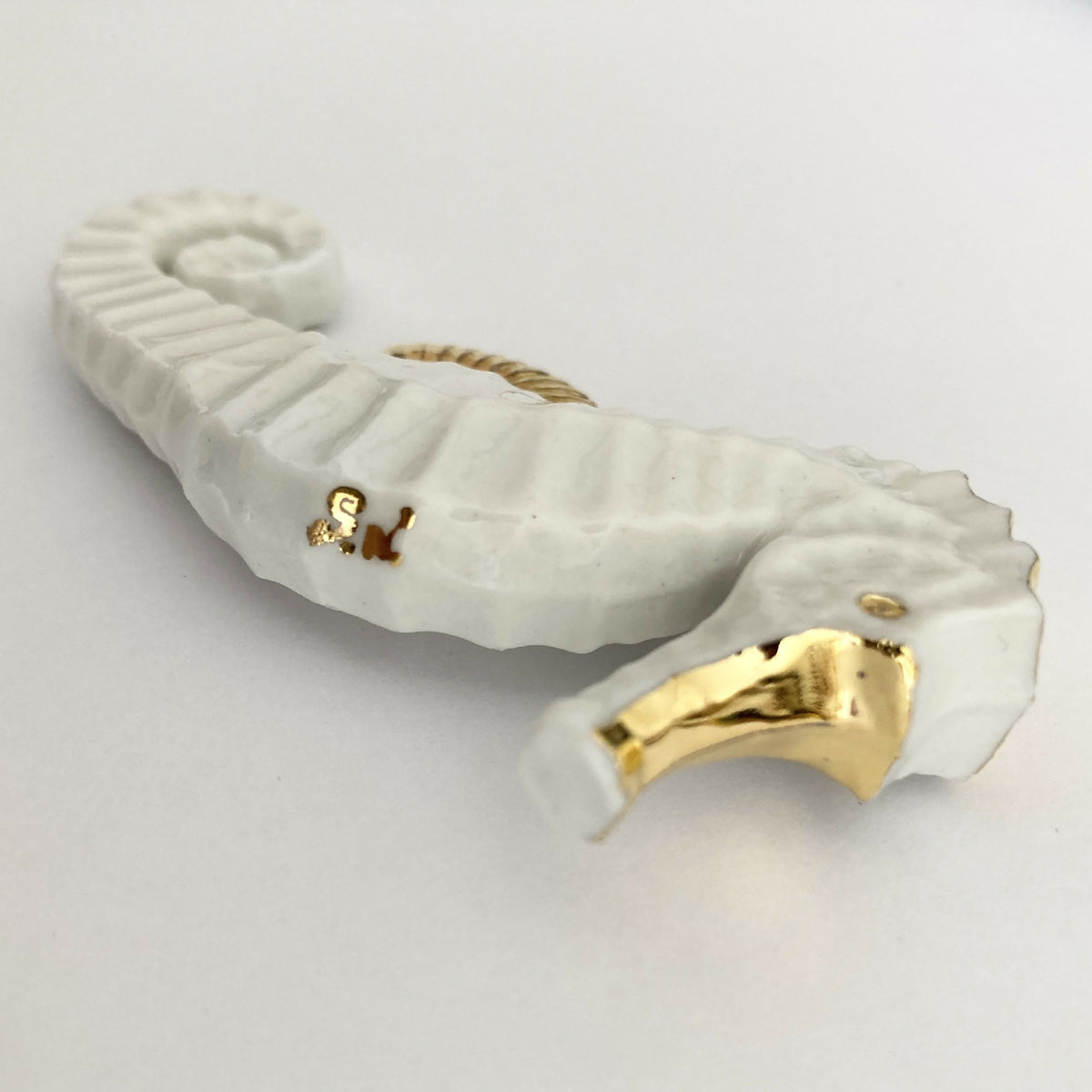 Porte-couverts hippocampe blanc avec accents dorés, vue latérale.