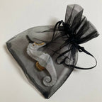 Porte-couverts hippocampe blancs et dorés dans un sachet en organza noir.