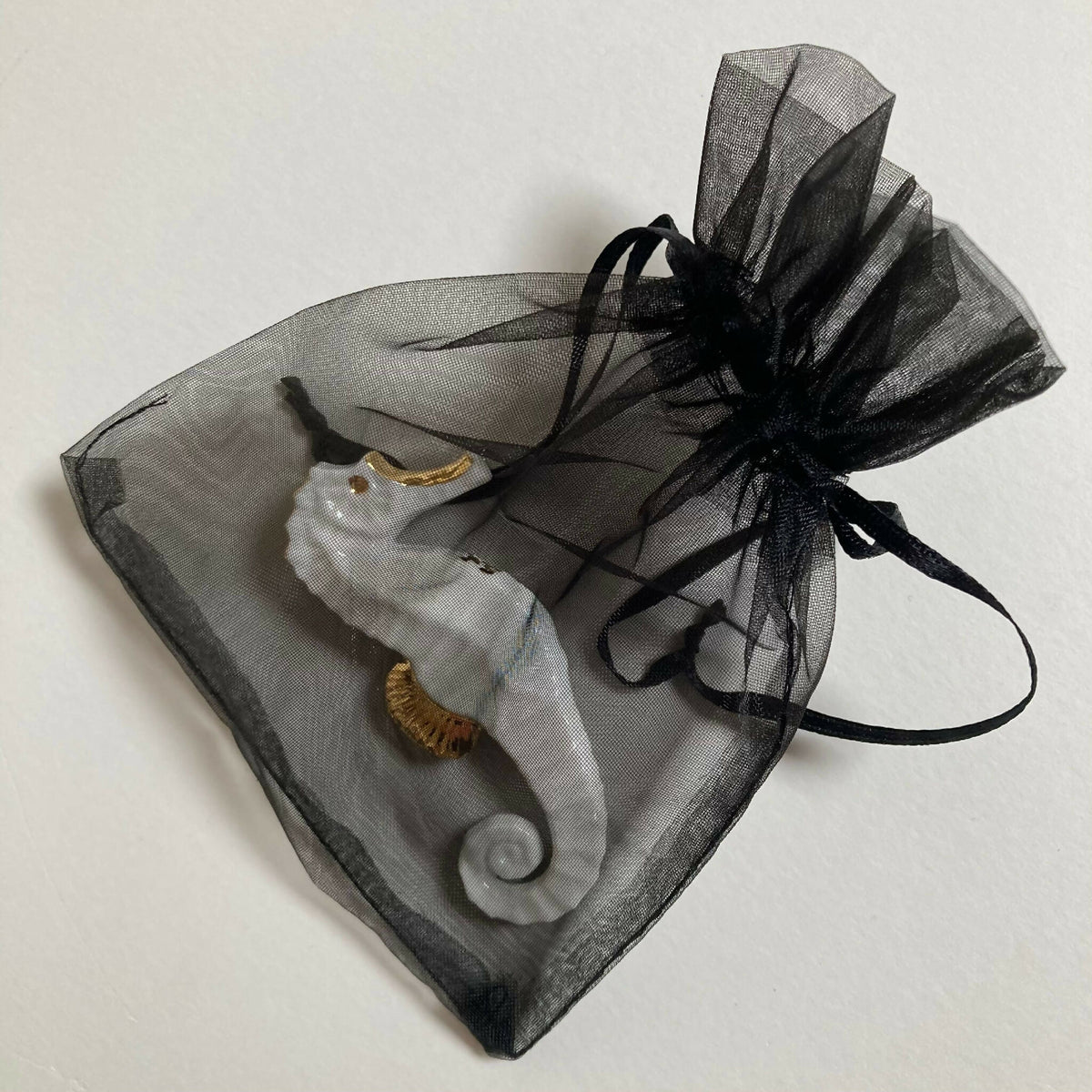 Porte-couverts hippocampe blancs et dorés dans un sachet en organza noir.