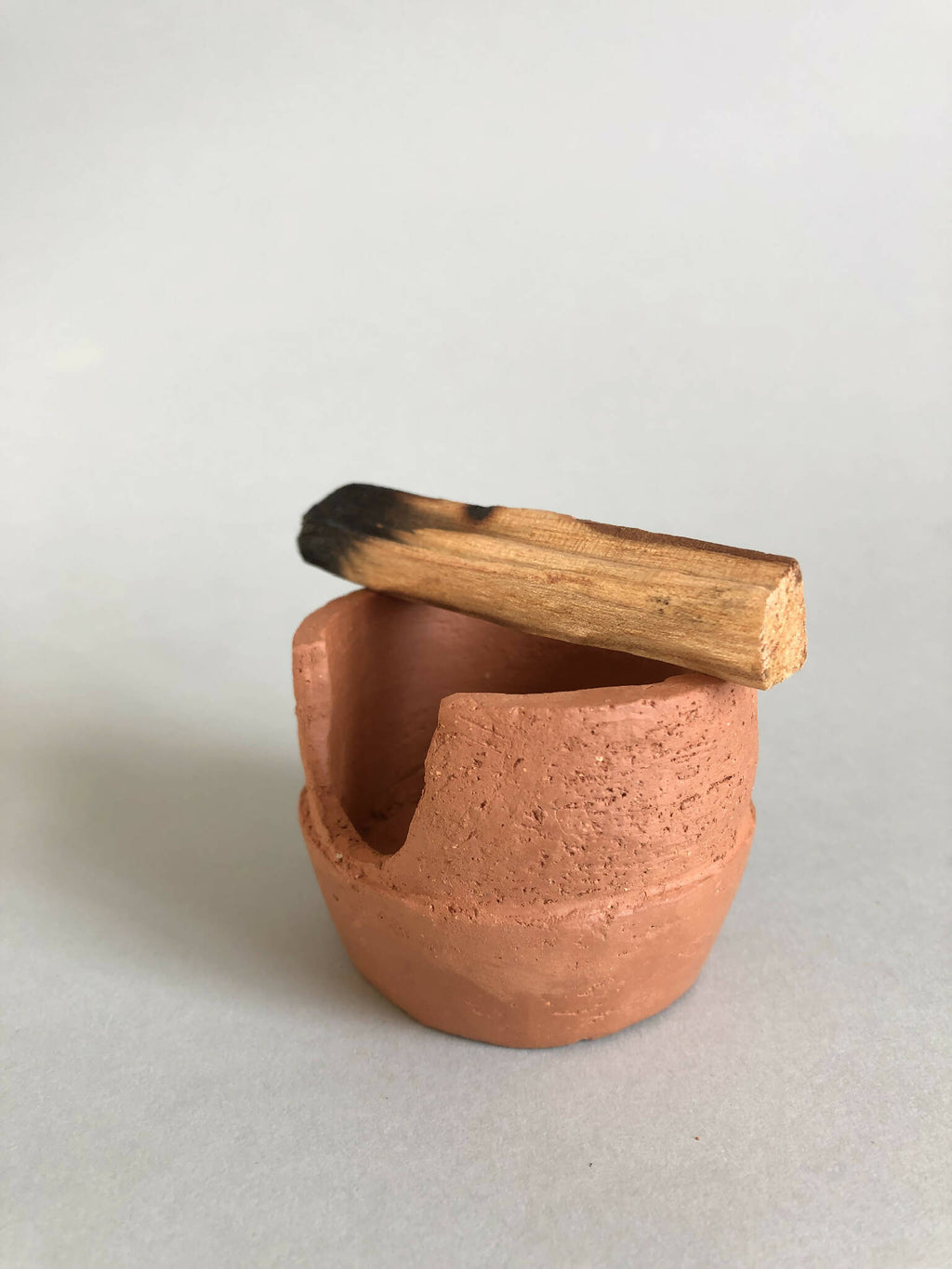 Petit pot en argile terracotta avec ouverture latérale et branche en bois.