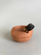 Petit pot en argile terracotta avec ouverture circulaire et pierre noire à l’intérieur