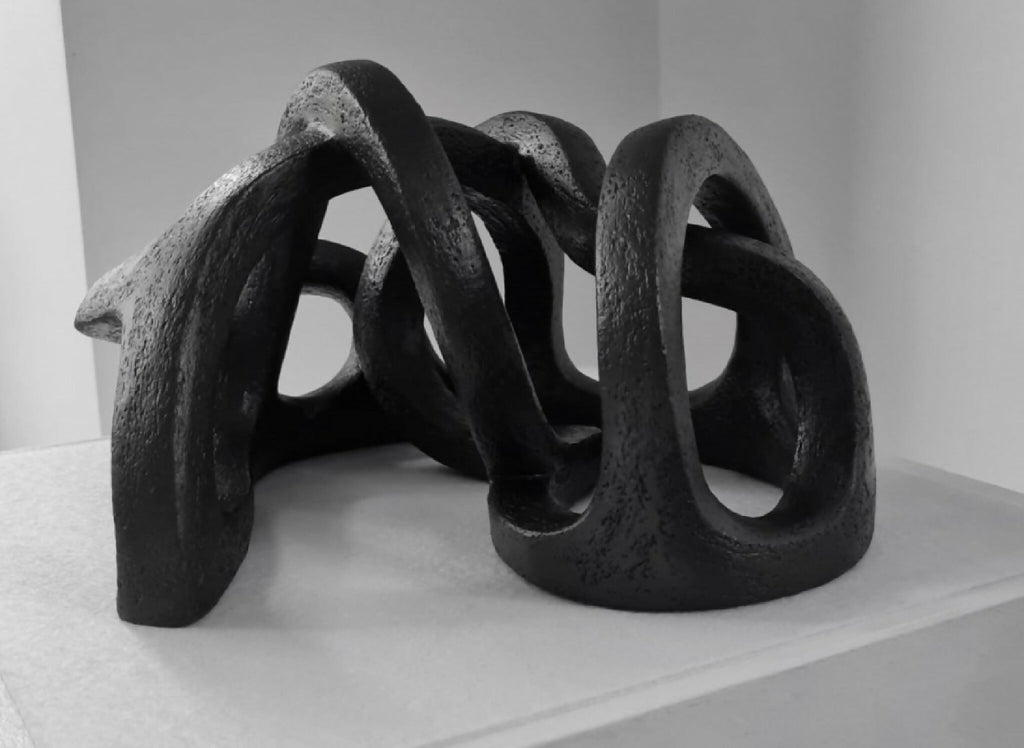 Sculpture abstraite en argile sombre, courbes entrelacées et appuis au sol.