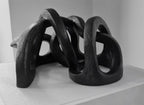 Sculpture abstraite en argile sombre, courbes entrelacées et appuis au sol.