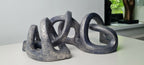Sculpture abstraite gris bleuté, formes circulaires enchevêtrées sur socle.