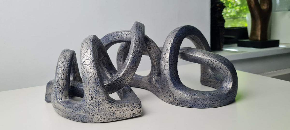 Sculpture abstraite gris bleuté, formes circulaires enchevêtrées sur socle.