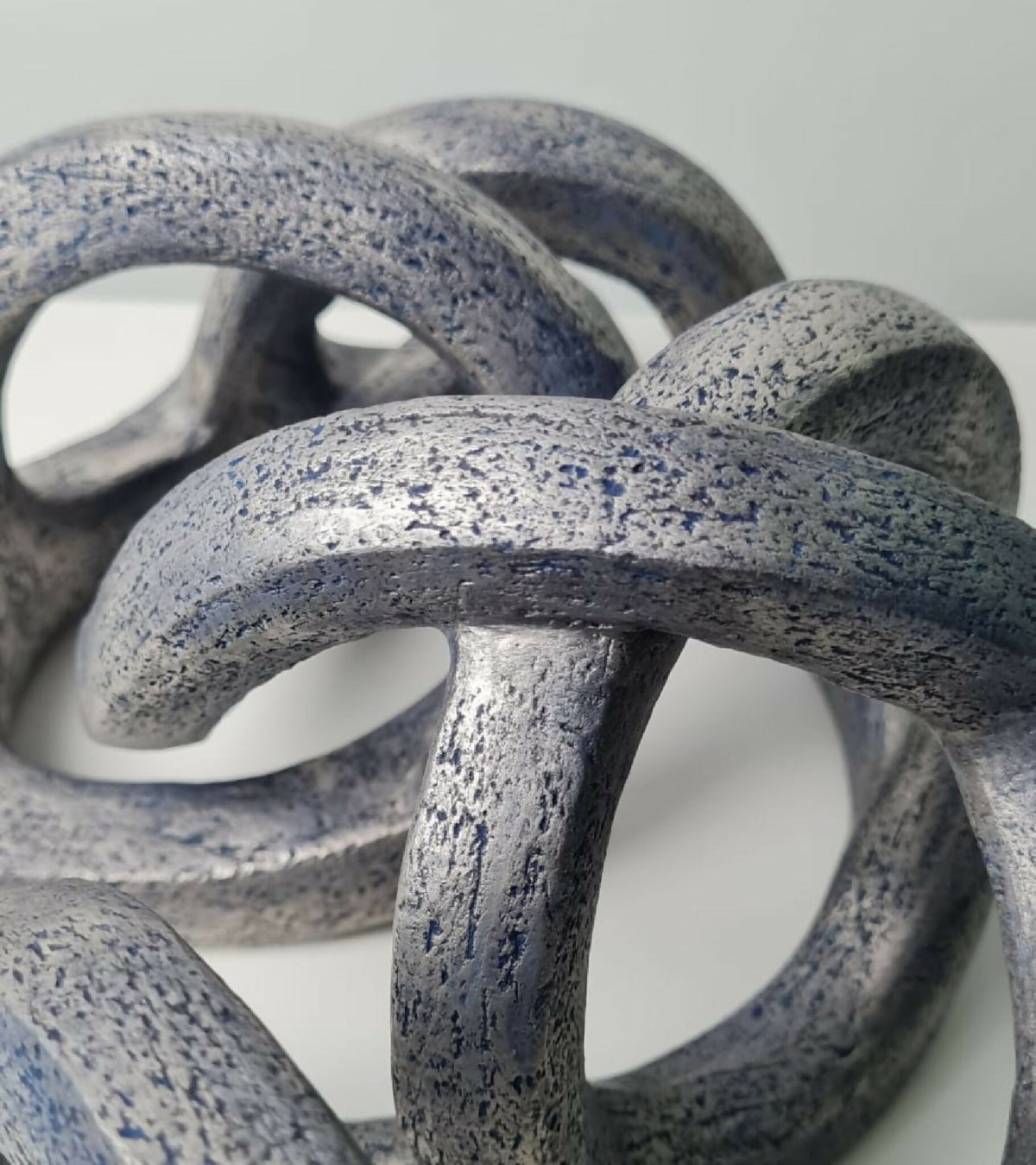 Courbes enchevêtrées de la sculpture abstraite, texture granuleuse avec points bleus.