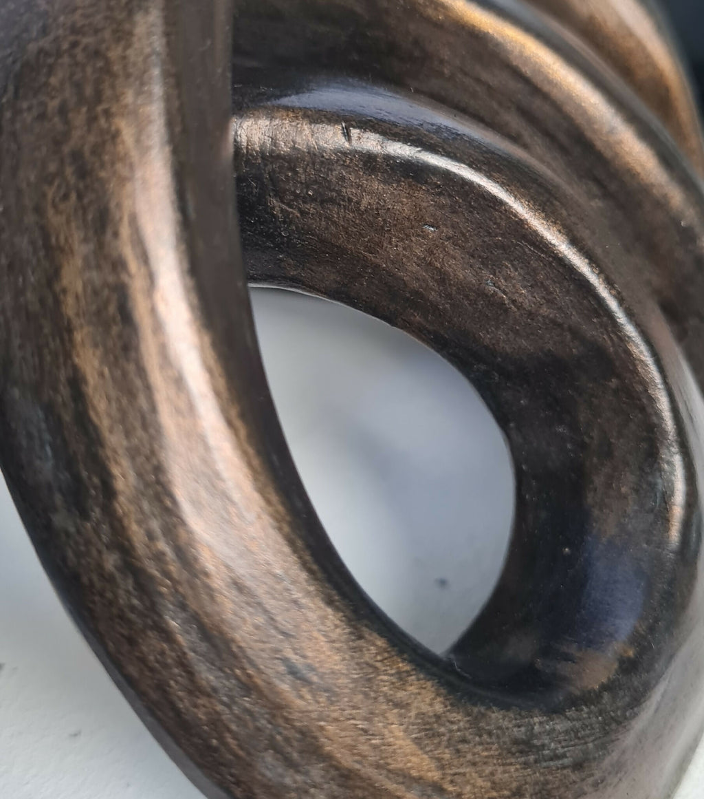 Détail de sculpture abstraite : anneaux métalliques sombres et reflets cuivrés